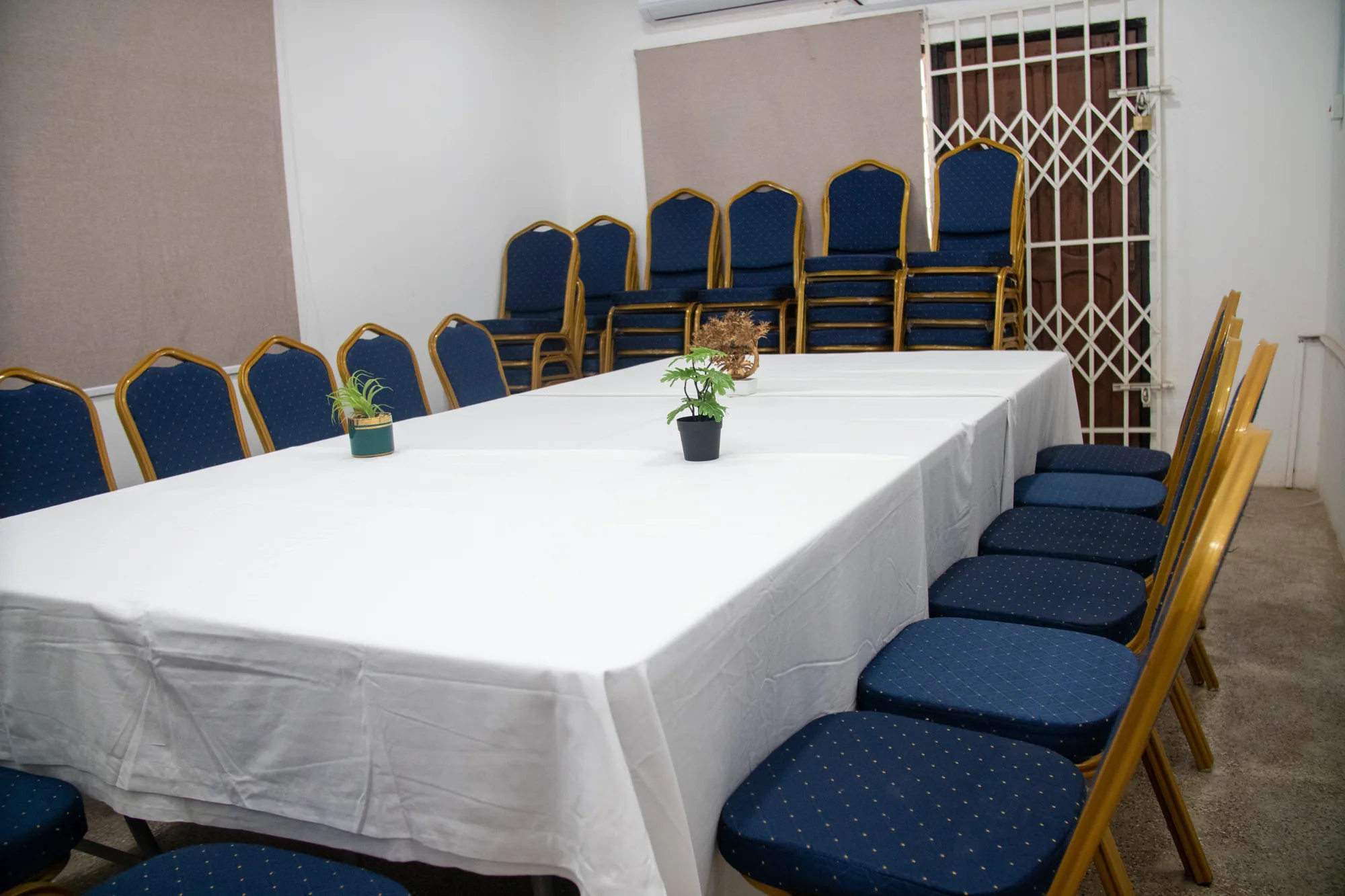 Conference tables with white linens, blue and gold chairs and greenery at yecSpace